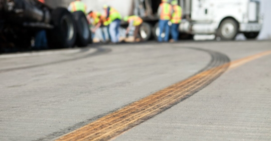 A semi tractor and trailer has crashed on a highway and workers are cleaning up the scene.