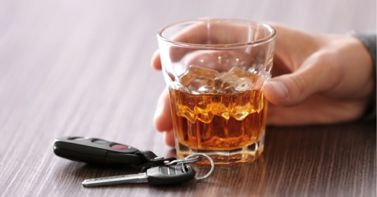 Man with an alcoholic drink in his hand and his car keys next to the drink.