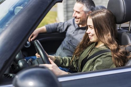 A teenage girl driving a car with her father